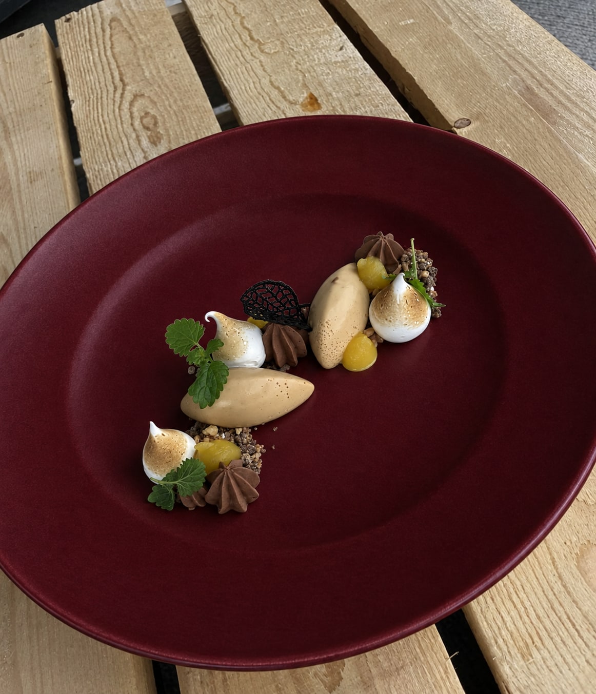 A plated dessert with meringue, chocolate and fruit on a burgundy plate